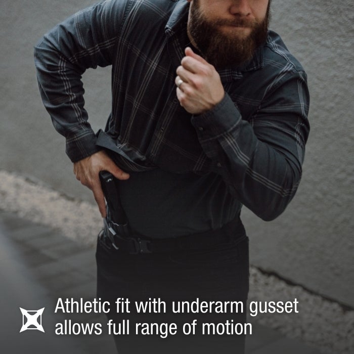 Photograph of a man drawing a handgun from his waistband outdoors wearing a dark plaid shirt and black pants his hand displaying a ring