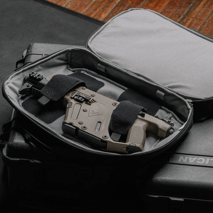 Photograph of a tan and black firearm secured with straps inside a black backpack on a wooden surface featuring a textured grip and a distinctive triangular logo