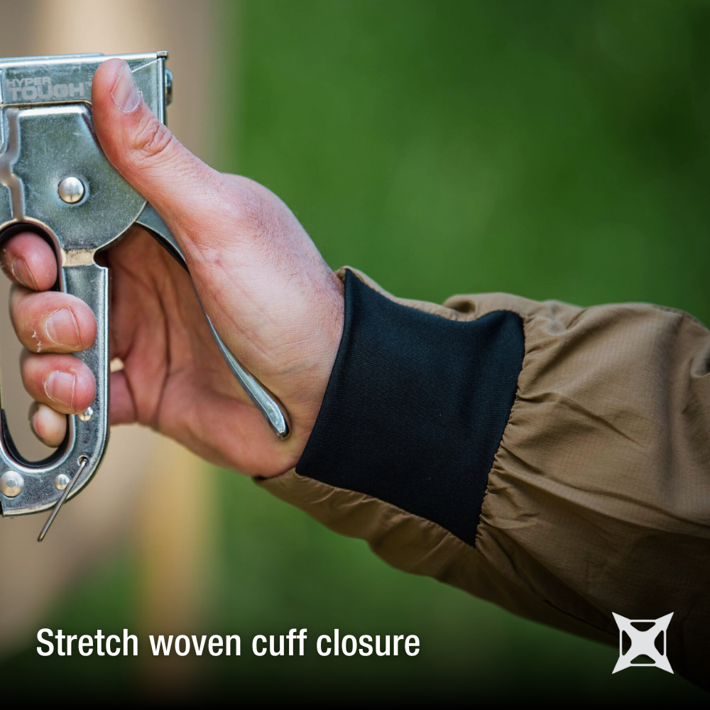 Product shot showing a hand holding a Hyper Tough staple gun against a blurred green background showcasing a tan shirt with black stretch woven cuff closure details