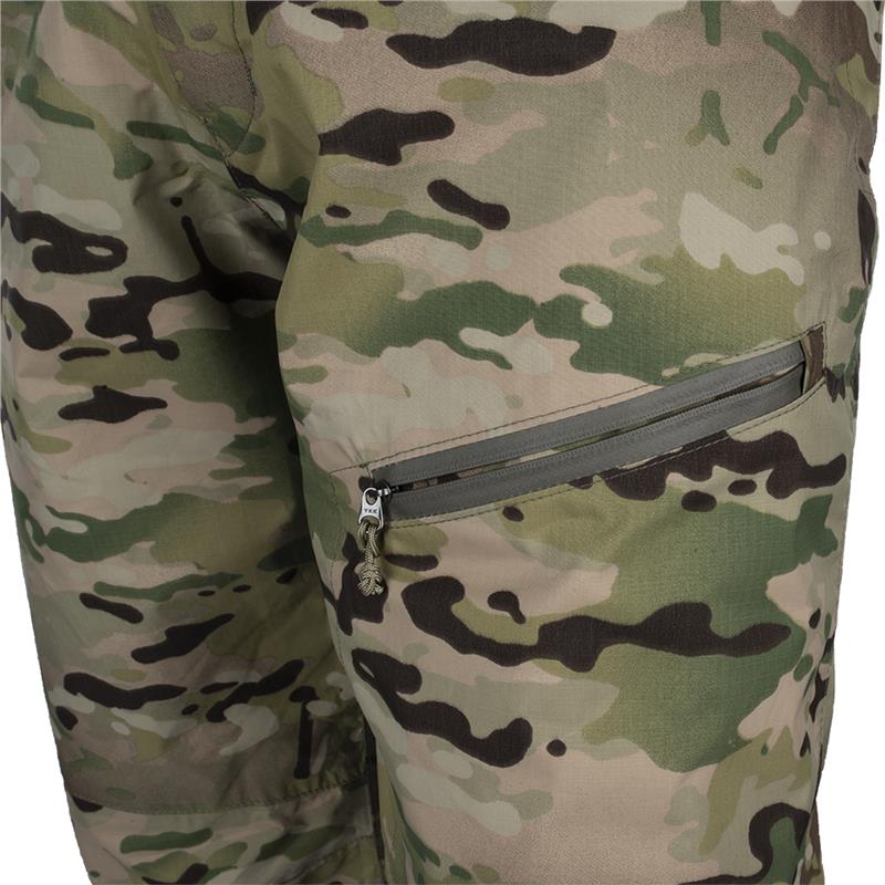 Close-up detail shot of camouflage fabric pants showing a zippered pocket with a decorative pull and muted greens browns and tans