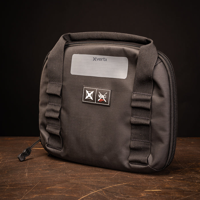 Product photography of a black Xvertx range bag on a dark wooden surface featuring a silver nameplate and black and red logo patches