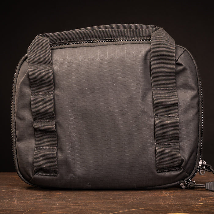 Product shot of a black nylon carry bag with zippered closures and adjustable straps on a dark wooden surface showing textured fabric and robust stitching