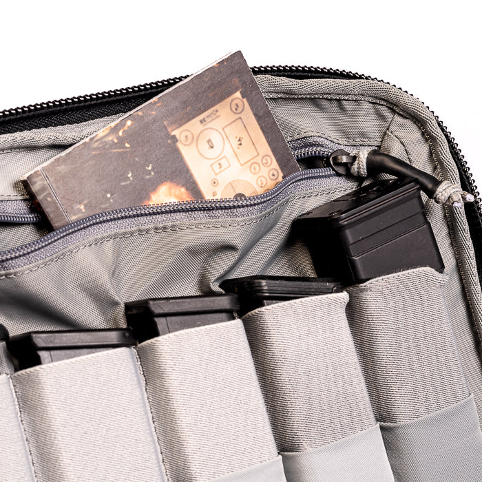 Photograph of a gray tactical bag containing multiple black rifle magazines a notebook with a stylized explosion and control panel design and a gray zipper pull