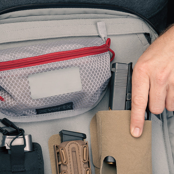Photograph showing a grey bag with a handgun and magazine pouches a red zipper a tan holster and a grey mesh pocket