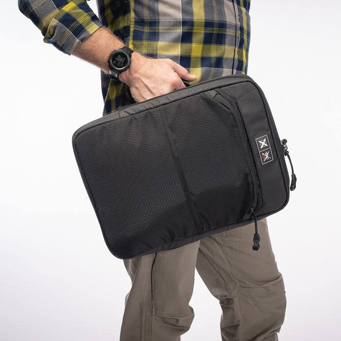 Product photography showing a person holding a black laptop sleeve with mesh detailing and branded patches against a white background