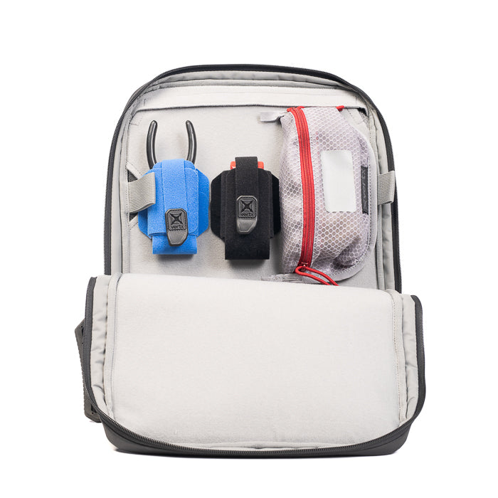Product photography shows the interior of a black backpack with a gray lining containing a blue and black pouch a red zippered pouch and other accessories