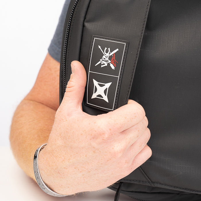 Close-up photograph showing a person holding a black VIC FIRTH drum bag featuring a logo with crossed drumsticks a red accent and a geometric pattern the bag is made of textured fabric with subtle stitching
