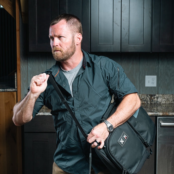 Photography unknown artist a man with a beard in a dark green shirt carrying a black bag in a modern kitchen with dark cabinets and granite countertops