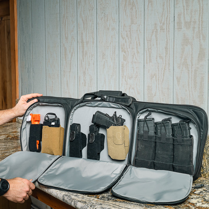 Photograph showing a black gun range bag with holsters, pistol, magazines, and orange accessories on a countertop against a wood-paneled wall.