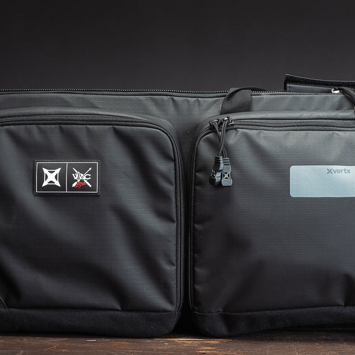 Product Photography XVertx black dual-compartment bag with zipper pulls and logo patches on dark wood surface.