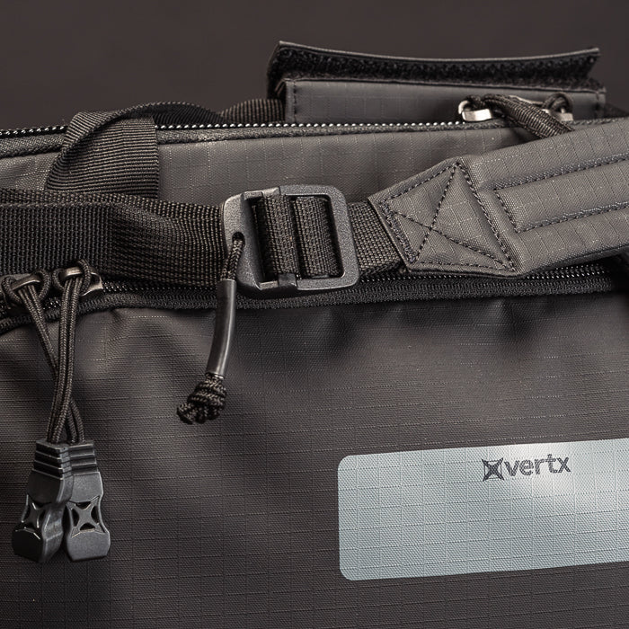 Product shot of a Vertx black duffel bag featuring a textured fabric, a black plastic buckle, and cord pulls with unique plastic ends