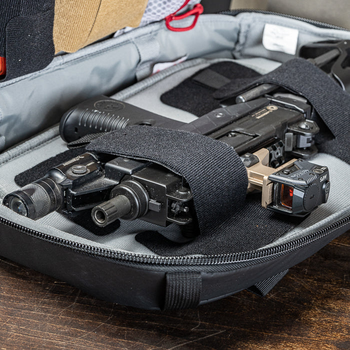 Photograph of a black submachine gun with tan and red accents secured in a gray carrying case on a wooden surface