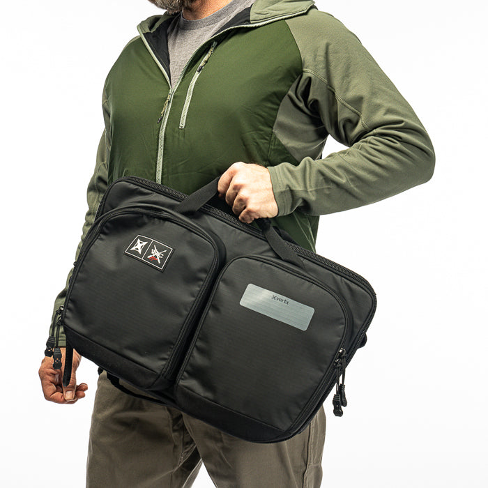 Product shot showing a person holding a black XVERTIX range bag featuring dual compartments a logo patch and a silver label against a white background