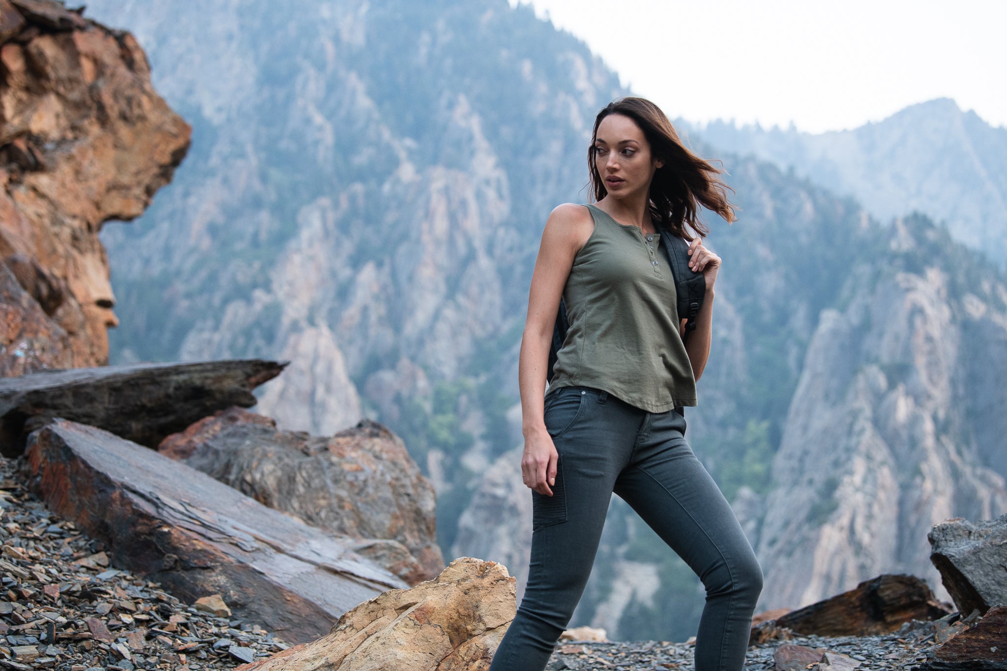 Photography Unknown Woman hiking among dramatic rock formations and mountains featuring a brown and grey color palette and a woman wearing a olive green tank top and dark grey pants