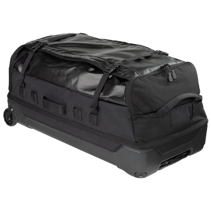Product shot of a black wheeled duffel bag featuring compression straps, a top carry handle, and durable wheels on a dark gray base