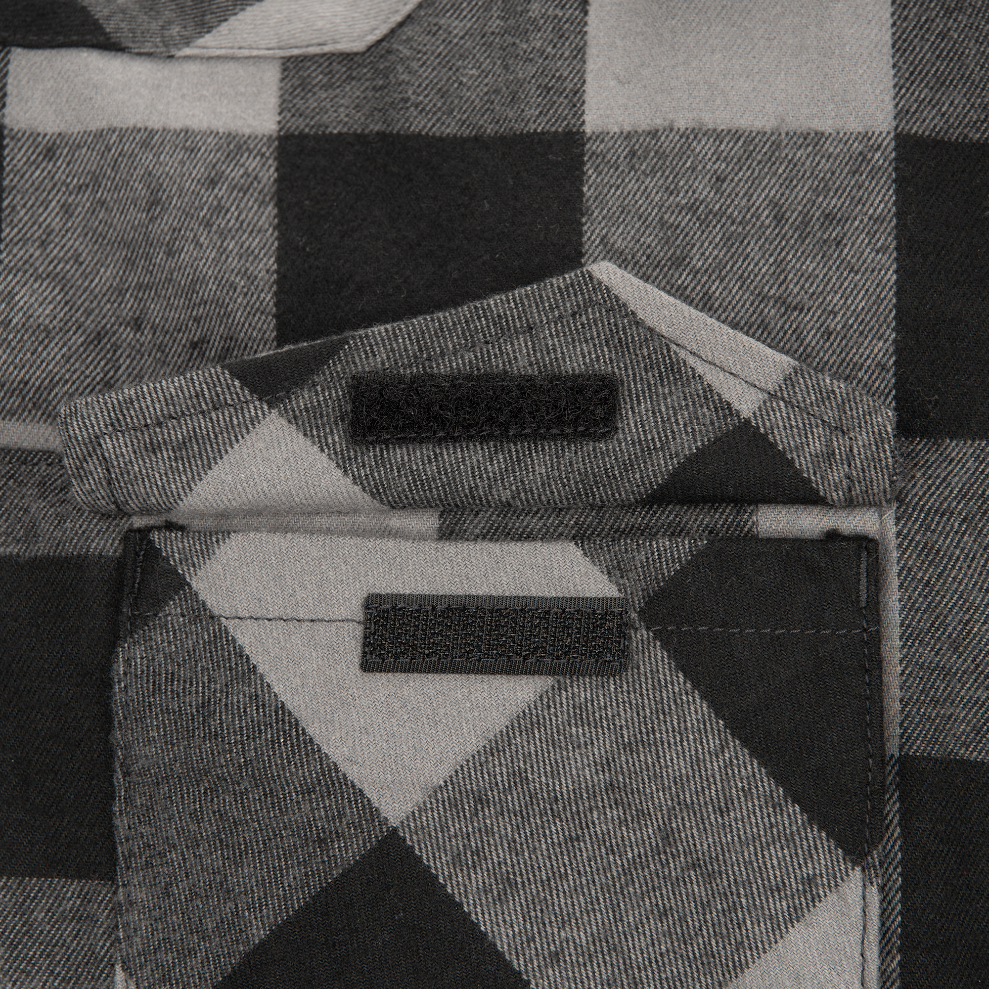 Close-up of a gray and black plaid flannel shirt pocket featuring black hook and loop fasteners and subtly textured fabric
