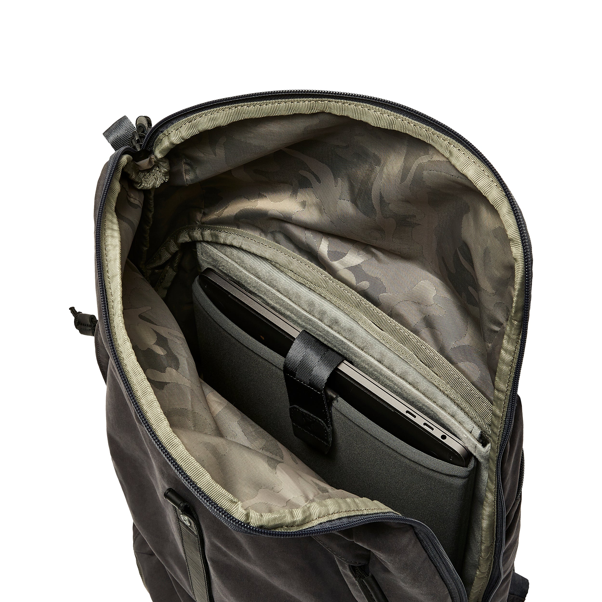 Product shot showing the interior of a dark gray backpack featuring a padded laptop sleeve, olive green lining with a subtle camouflage pattern, and black zipper pulls