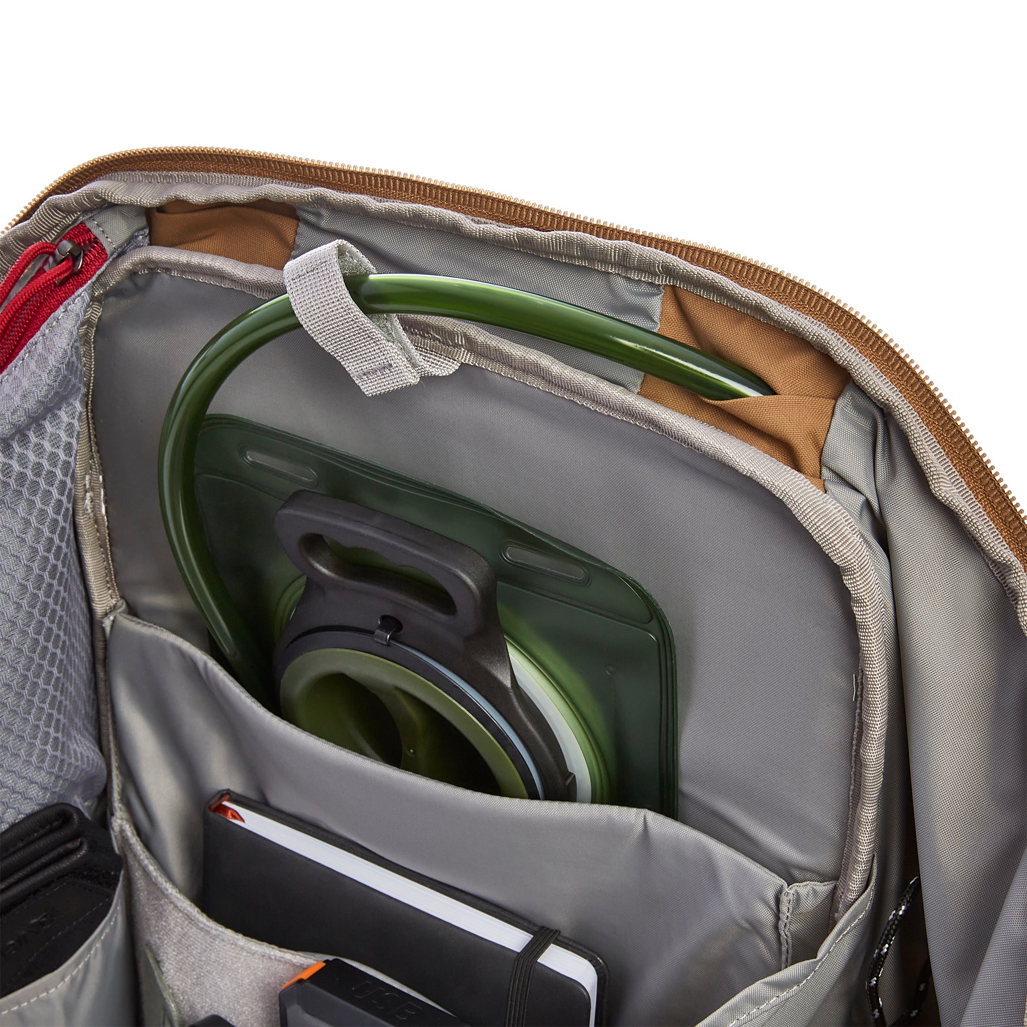 Interior of a durable backpack showing a green hydration bladder, a black notebook, and a contrasting brown zipper with a red pull cord