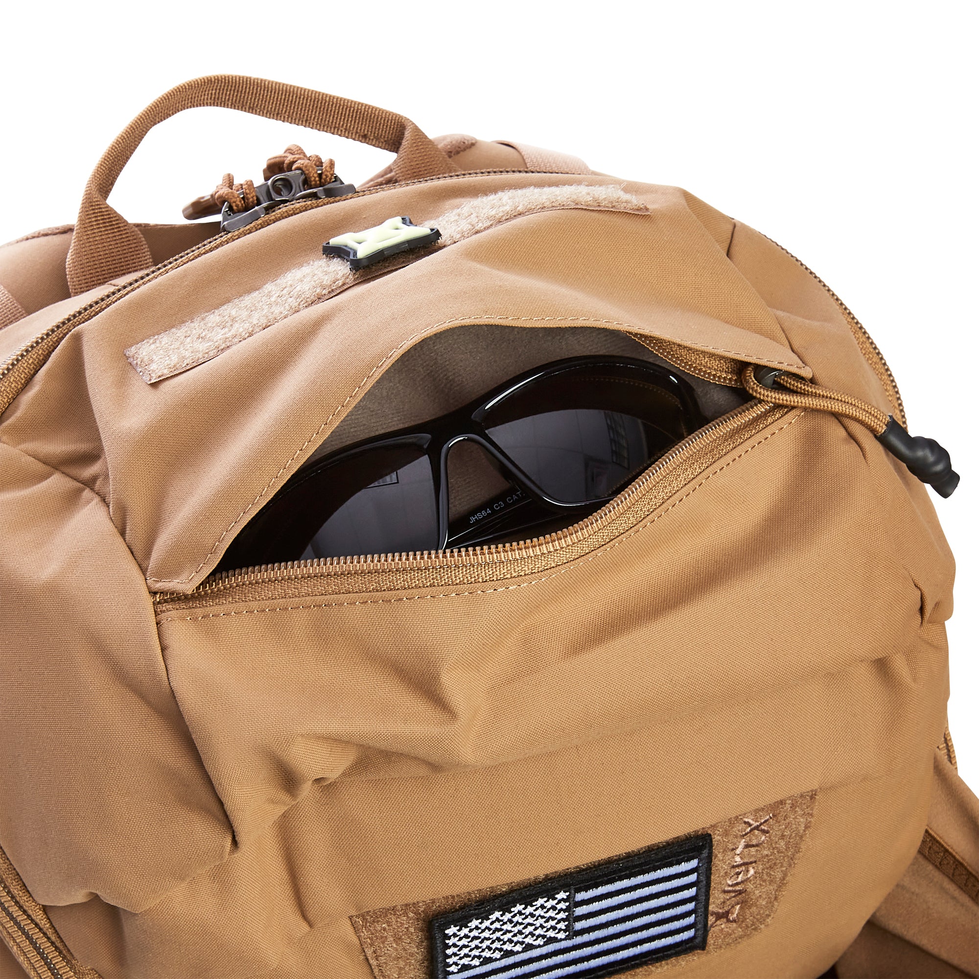 Close-up of a tan Vertx tactical backpack with black sunglasses in its open zippered pocket and a black and blue Thin Blue Line American flag morale patch on a Velcro panel