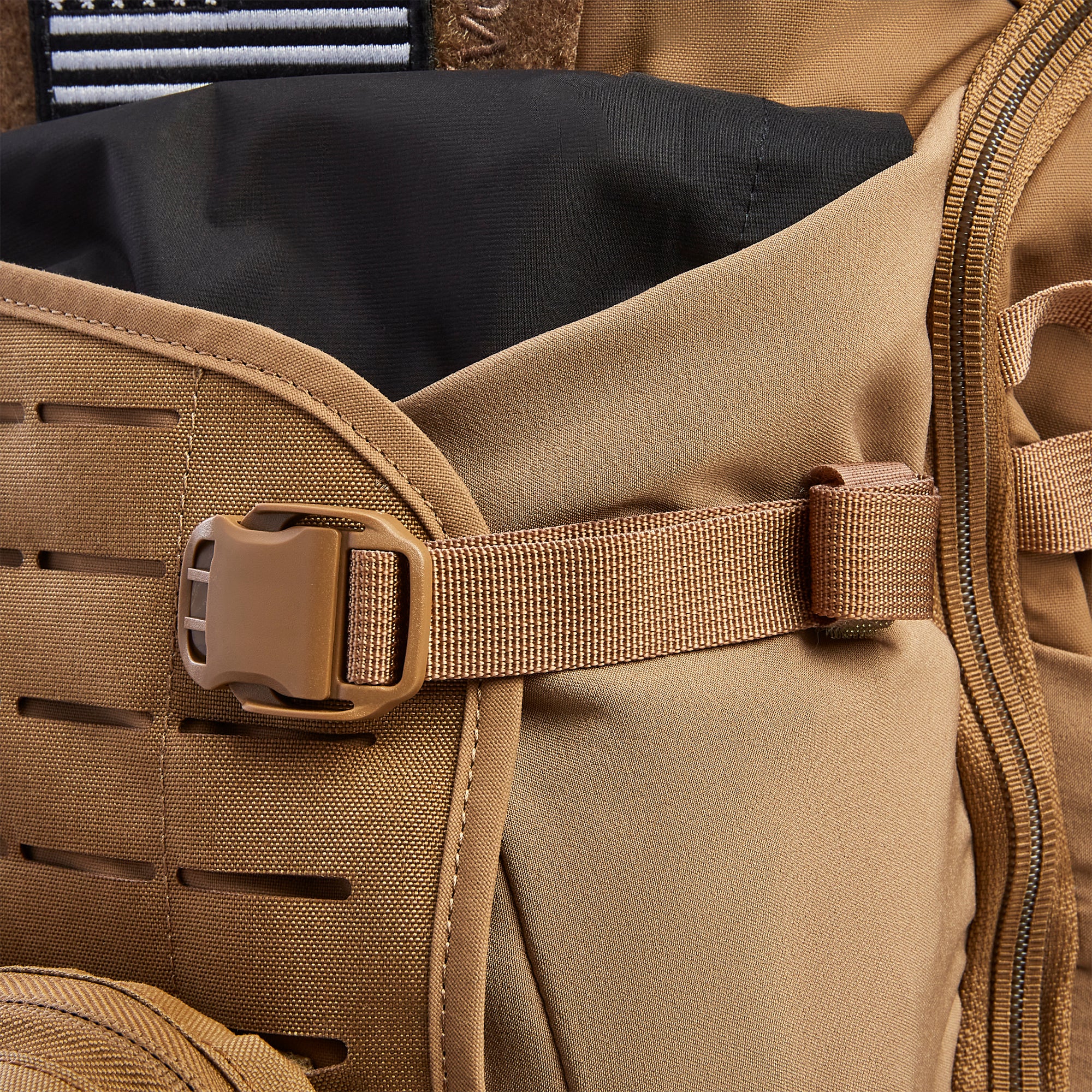 Close-up of a coyote brown tactical backpack with a tan plastic buckle, a black interior lining, and a white striped patch