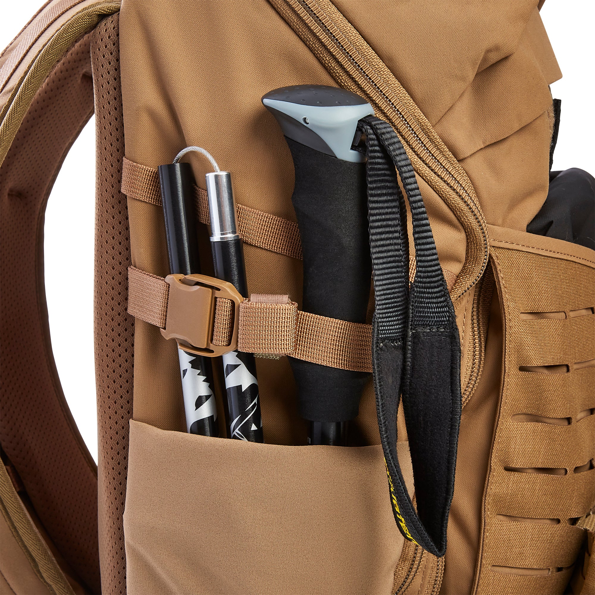 Tan hiking backpack side pocket holding black and silver trekking poles secured by a brown buckle and featuring black mesh padding and MOLLE-style webbing
