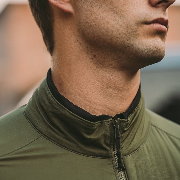 Close-up photograph showing a man's neck and olive-green zip-up jacket with black inner collar and subtle texture detail