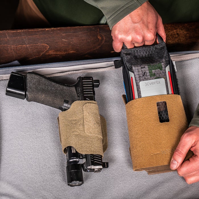Photograph showing a Glock handgun in a tan holster and a Vertrx device in a tan pouch inside a gray carrying case with a textured fabric and a black flashlight attached to the gun