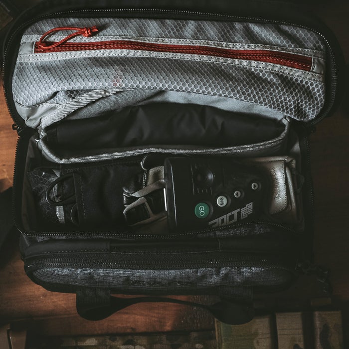 Photograph of a gray and black travel bag containing gloves, a device with a green GO button, and a red zipper detail on a wooden surface