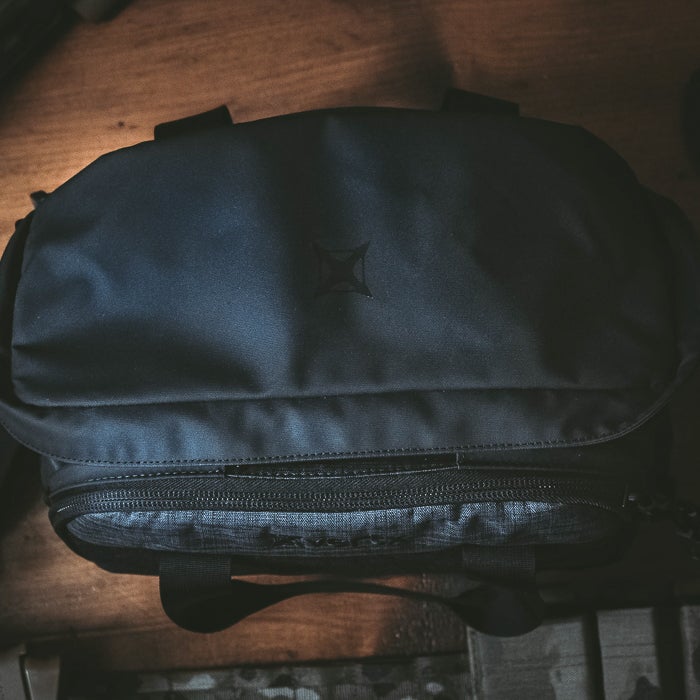 Photograph of a dark blue Jansport bag featuring a subtle embossed logo a contrasting gray zipper and sturdy black handles resting on a wood surface