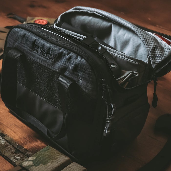 Photograph of a dark gray and black Averix range bag on a wooden surface showing a gray interior zippered compartment and textured fabric details