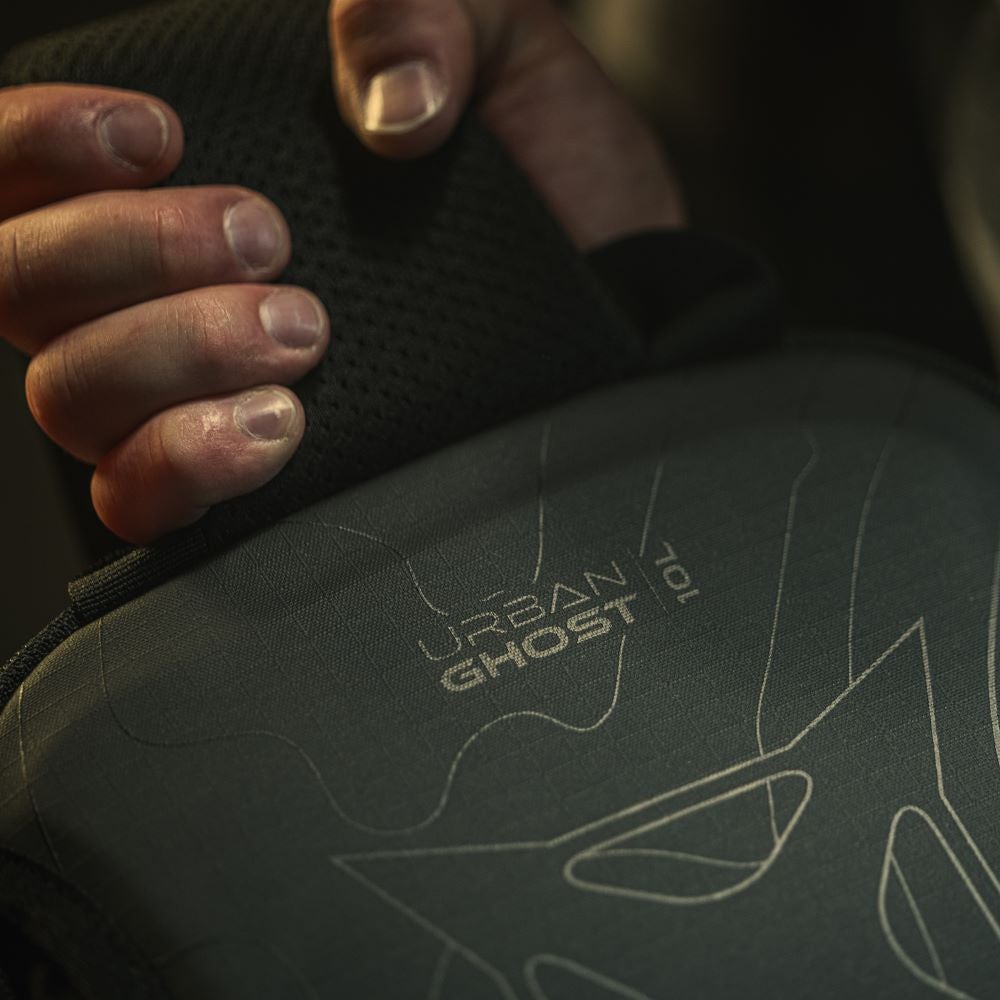Close-up product shot of a dark-green Urban Ghost 10L backpack showing its breathable mesh back panel and embossed design featuring light-grey topographical lines and branding details