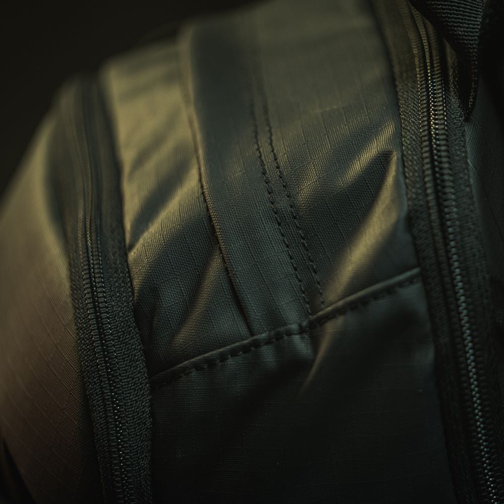 Close-up photograph of dark green fabric showing subtle texture and stitching detail along zippers