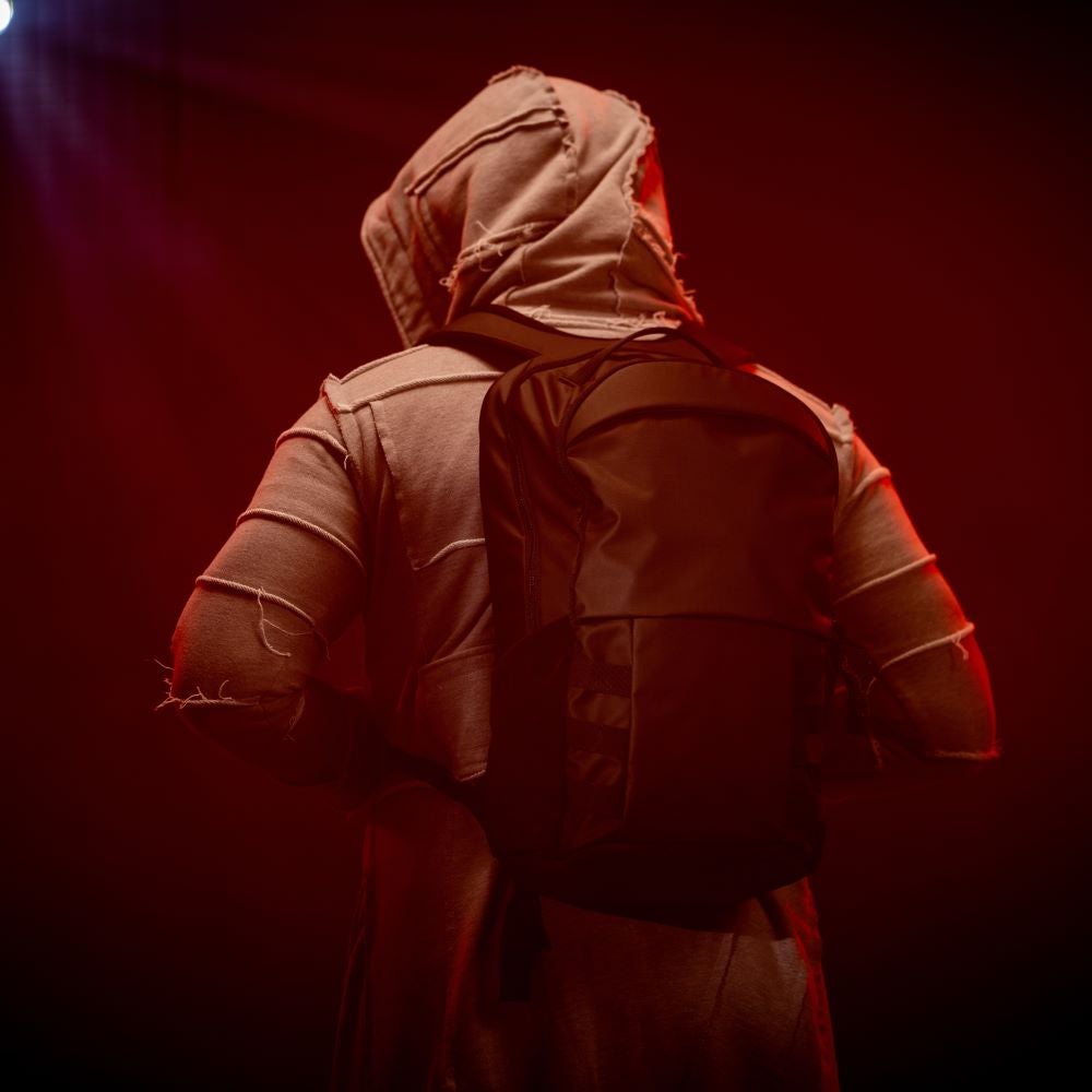 Photographic artwork of a person wearing a distressed grey hoodie and a dark backpack against a red backdrop featuring dramatic lighting and a textured fabric