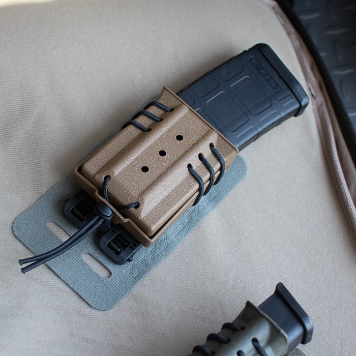 Product photography showing a tan polymer AR-15 magazine pouch with black paracord lacing and a black magazine on a gray backing featuring subtle texture and a unique closure system