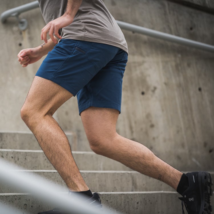Photograph of a man in dark blue athletic shorts running up a concrete staircase showing hairy legs and a small tattoo near his ankle alongside a grey handrail