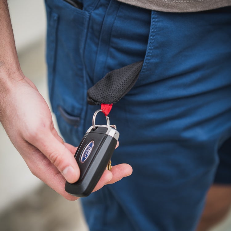 Photograph of a hand holding a Ford car key attached to a black and red key holder clipped to blue shorts.