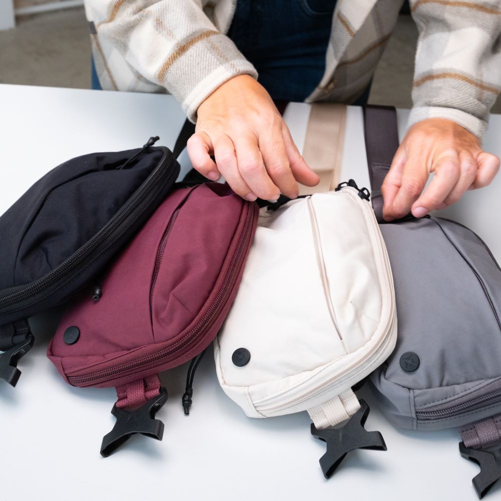 Photograph showing four crossbody bags in black, burgundy, cream, and gray on a white surface each bag features a unique zipper and clasp detail