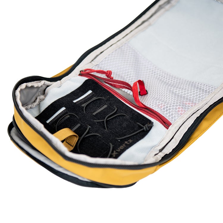 Product shot showing the mustard yellow interior of a Vertex pack with a black organizational panel, red zipper pulls, and grey mesh pockets