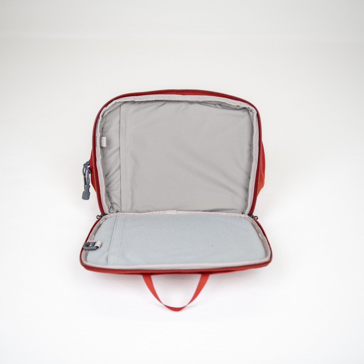 Product photography of an open red zippered carrying case with grey interior pockets and a small red handle showing organizational features