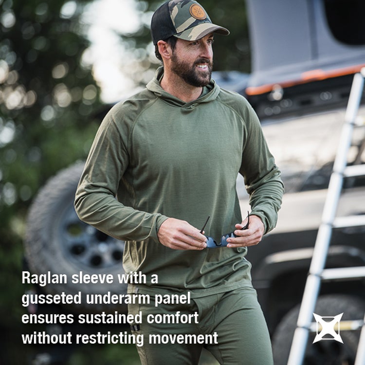 Photography of a man in a green long-sleeve shirt and camouflage hat outdoors near a vehicle and ladder with sunglasses in hand showing raglan sleeves and a gusseted underarm panel