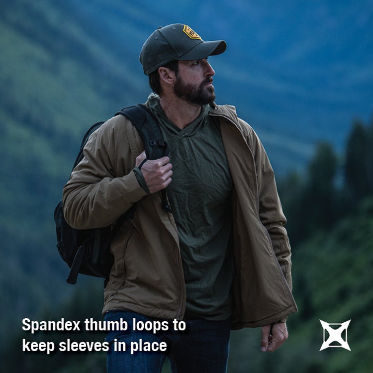 Photography Unknown man in tan jacket and green shirt hiking in mountains with dark blue sky and lush green vegetation featuring a dark green backpack and a yellow and gold logo on his cap