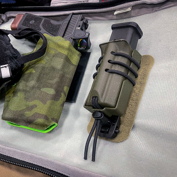 Photograph showing a handgun in a camo pouch and a magazine in a green holster inside a gray bag featuring lime green accents and black bungee cords.