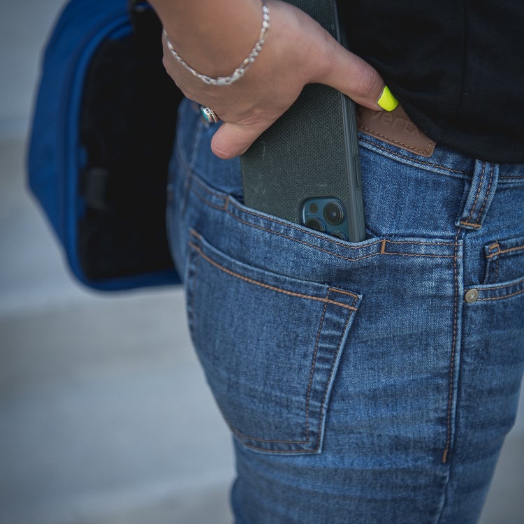 Photography unknown artist a person wearing blue jeans with a dark green phone in the back pocket a silver bracelet and bright yellow nail polish are visible