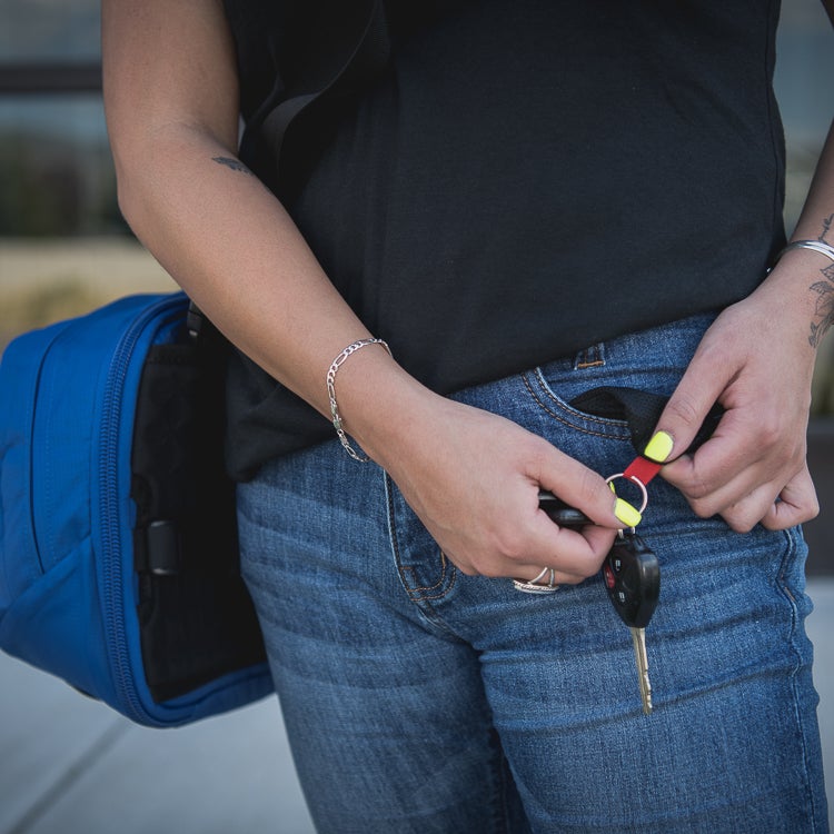 Photograph A woman wearing blue jeans and a black shirt adjusts her car keys featuring a red and yellow keychain detail while carrying a vibrant blue bag a silver bracelet and small tattoos are visible