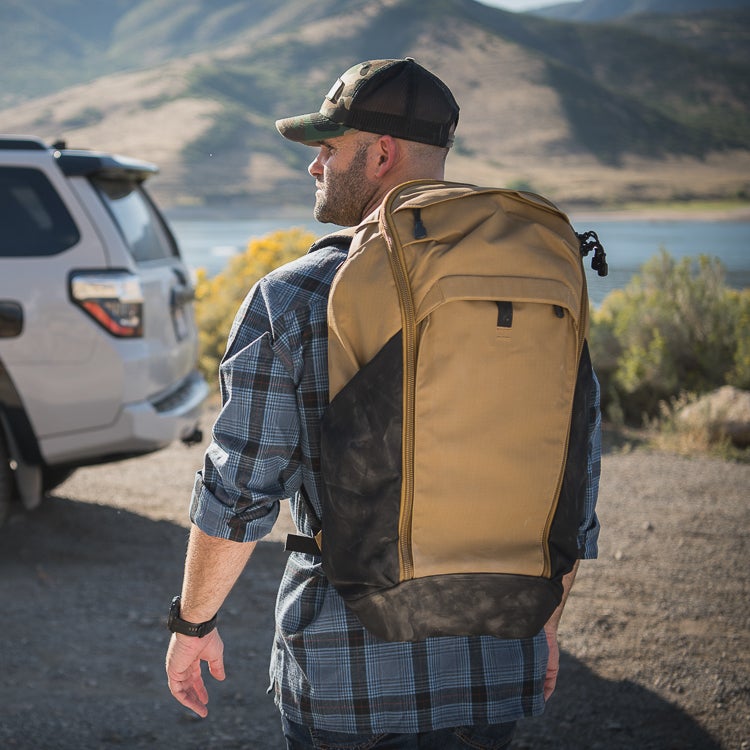 Photograph man tan backpack near lake and mountains wearing plaid shirt and camouflage hat