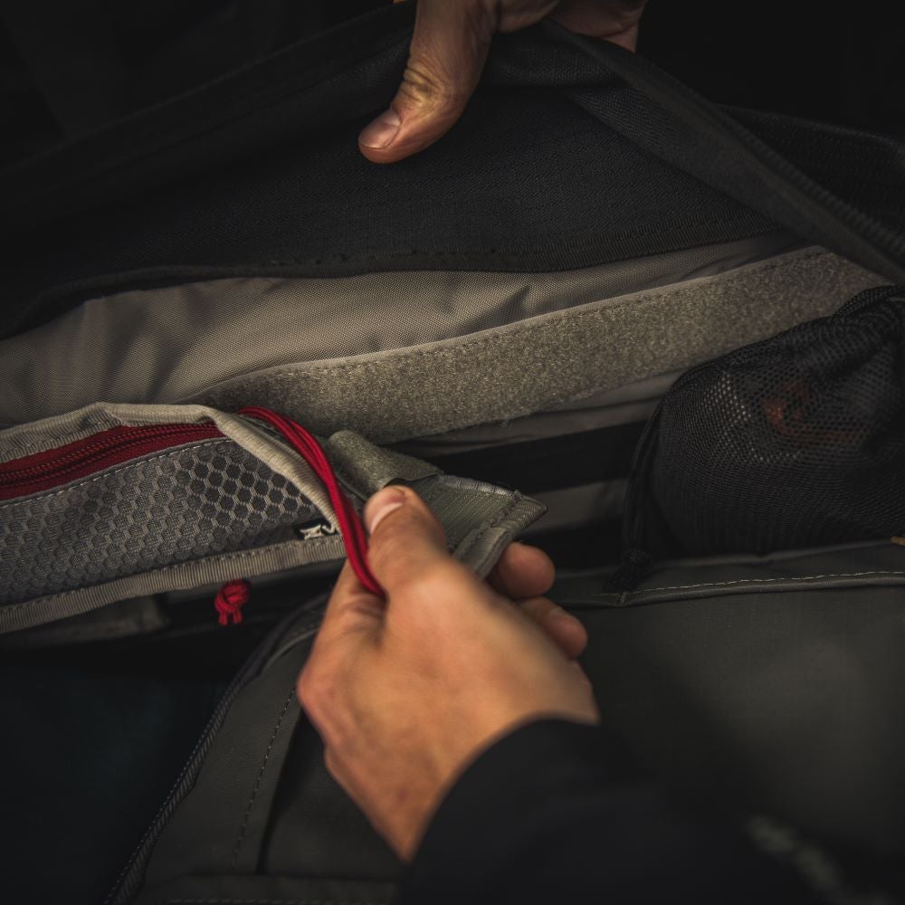 Photograph showing a detailed close-up of a gray and black backpack interior with red accents, a gray mesh pocket, and Velcro straps