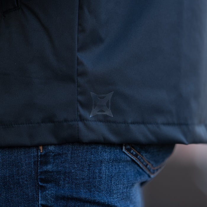 Product shot showing a dark navy blue jacket with a unique translucent logo detail on the lower back and the jacket is over a pair of denim jeans