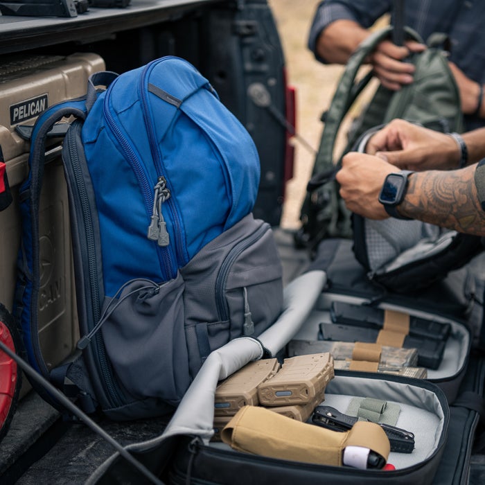 Photograph backpacks and tactical gear in a truck bed featuring a vibrant blue backpack tan pouches and gray and olive green tactical bags