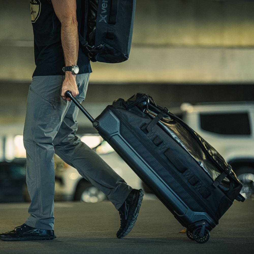 Photography Unknown artist A man pulls a wheeled duffel bag through a parking garage featuring gray concrete walls and blurred cars showcasing the bag's durable black fabric robust wheels and multiple compartments
