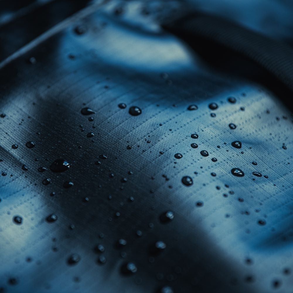 Close-up photograph showing water droplets on a dark blue waterproof fabric surface exhibiting varying sizes and reflective qualities